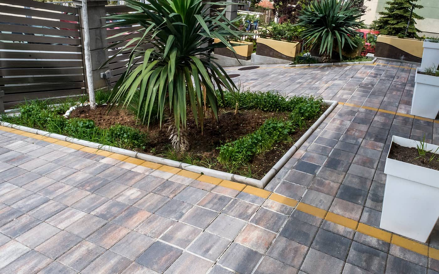 Dvorište sa lejom i žardinjerama popločano behaton pločama 20x20 u sivo-braon prelivima sa žutom trakom, model Holand 20x20