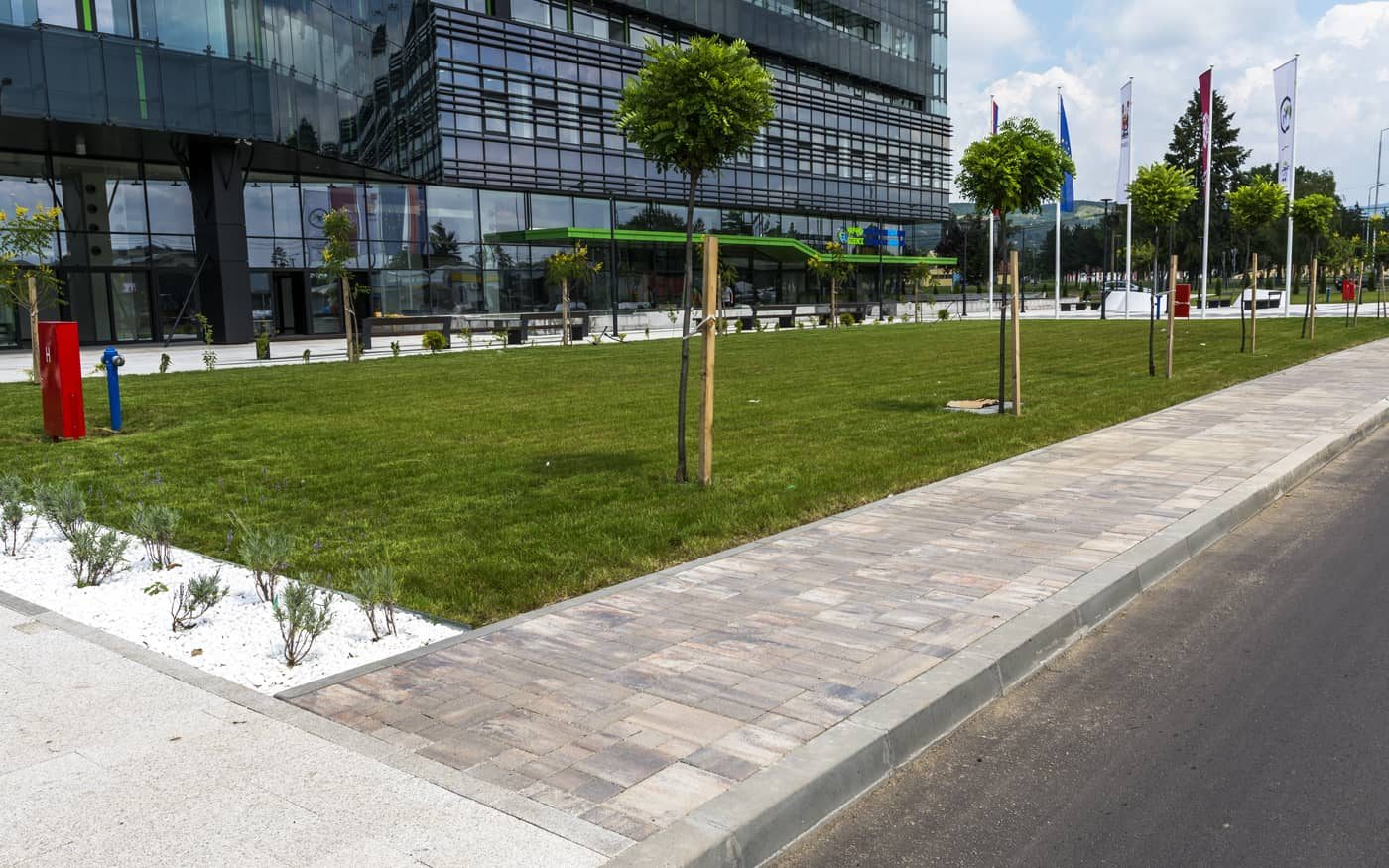 Trotoar uz travnjak ispred poslovne zgrade popločan behaton pločama u braon i sivim prelivima, model Kombo