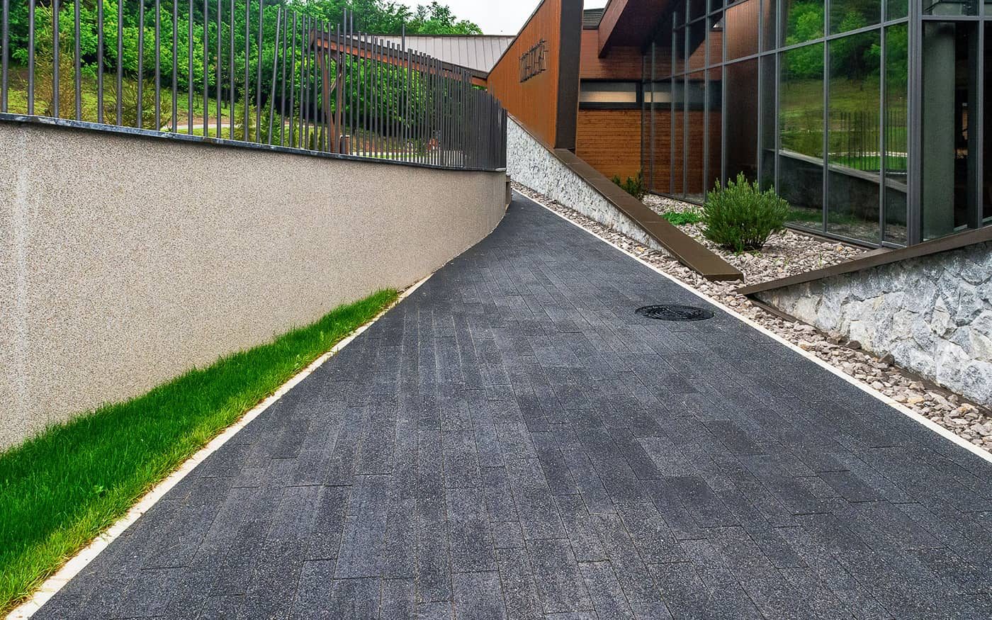 Kosa staza uz potporni zid i travnjak popločana tamno sivim behaton pločama, model Linea