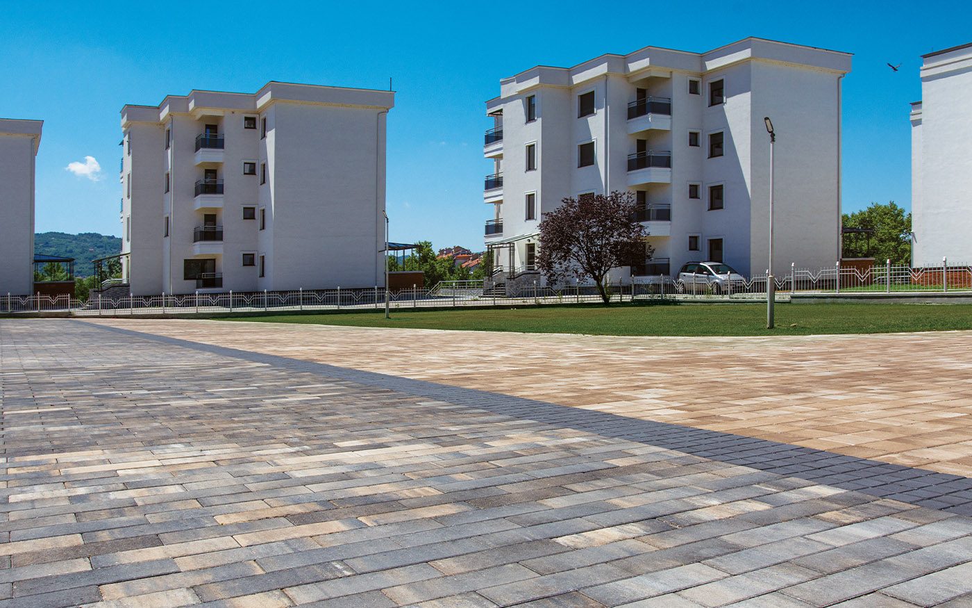 Plato ispred stambenih zgrada popločan izduženim behaton pločama u bež i sivim tonovima, model Modena