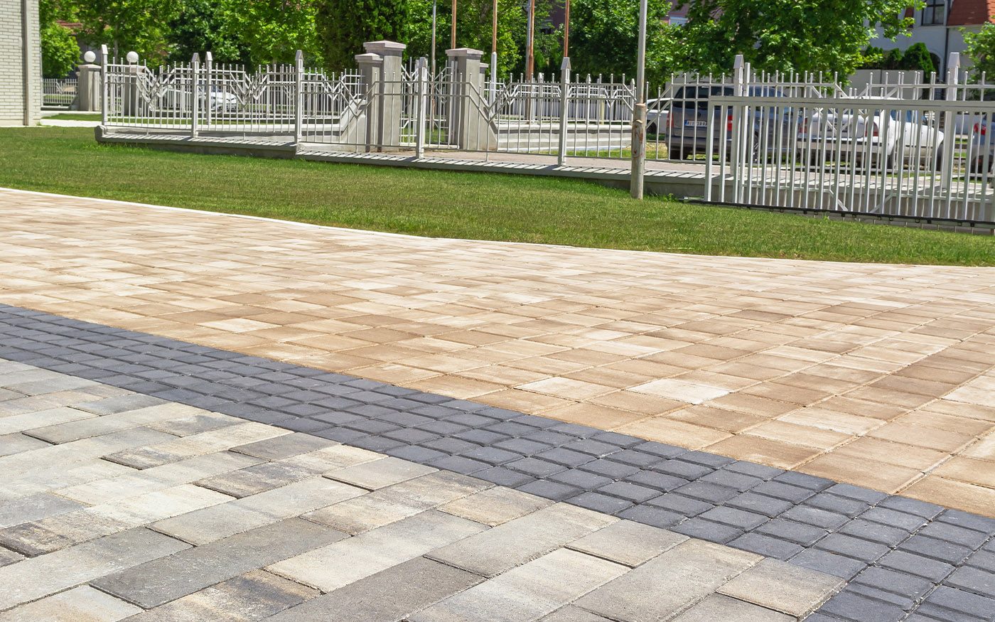 Plato uz travnjak i ogradu popločan bež i sivim behaton pločama sa tamnom trakom, model Modena