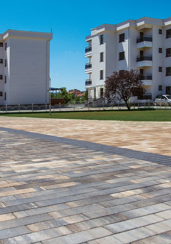 Plato između stambenih zgrada popločan izduženim behaton pločama u sivim i bež prelivima, model Modena